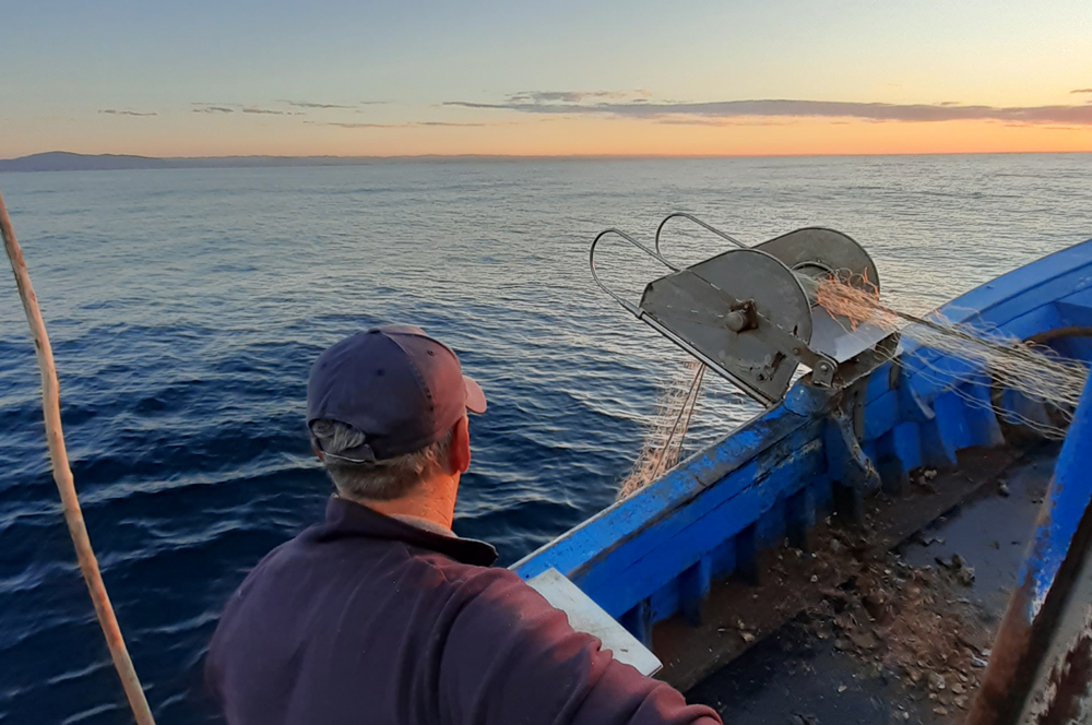pescador a içar mecanicamente as redes num barco de pesca